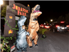 A child and adult dressed in inflatable t-rex costumes in front of a Jurassic Park themed display