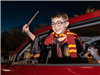 Boy dressed as Harry Potter with wand, scarf, and glasses, out car window smiling