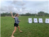 Teen girl preparing to toss a waterballoon at a row of targets on a soccer field.