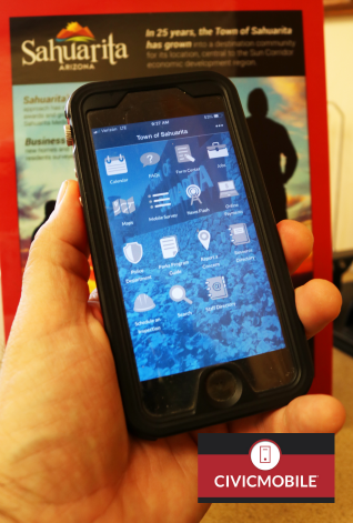 Photograph of cell phone in hand with Sahuarita advertisement in background